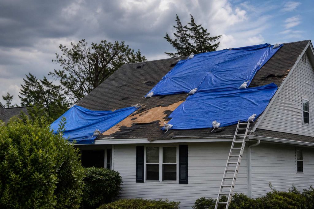 Residential roof with blue emergency tarps after storm damage under gray sky