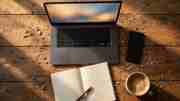 An overhead view of a laptop, smartphone, notebook, and coffee on a workbench scattered with wood shavings.